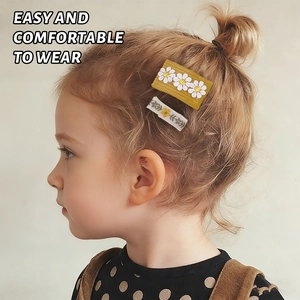 Détail de la broderie florale sur des barrettes en tissu jaune et blanc portées par un enfant