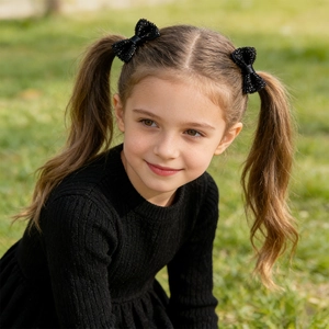 Dettaglio di fermagli per capelli a fiocco nero glitterato indossati da una bimba