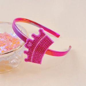 Glittery magenta rhinestone crown headband for girls on a warm beige background