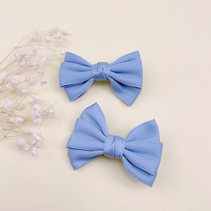 Détail de barrettes à nœuds bleu clair en tissu sergé sur un fond beige doux