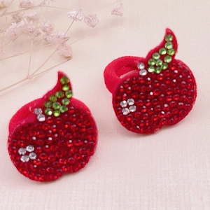 Pair of red rhinestone apple hair ties with green leaves on beige fabric background