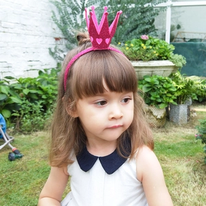 Girl wearing a sparkly pink glitter crown headband with hollow heart details in a garden