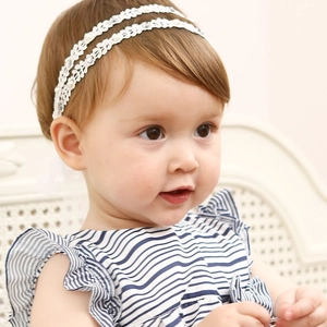 Détail d'un bandeau en dentelle pour bébé avec perles blanches fines et strass brillants