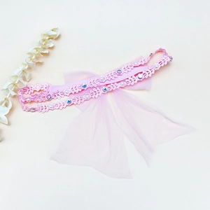 Détail d'un bandeau en dentelle rose avec gros nœud, perles blanches et strass bleus