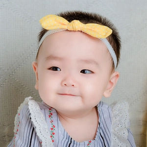 Close-up of baby lace headband featuring a yellow polka dot bow on a soft fabric texture