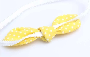 Close-up of yellow polka dot bow on white lace elastic headband for infants