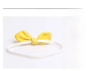 Detail of yellow polka dot bow headband for infants with a flexible elastic white band