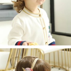 Close-up of white knitted baby cardigan with gold buttons and shiny headband detail