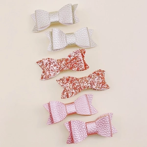 Close-up of handmade bow hair clips in litchi texture leather and glitter fabric styles