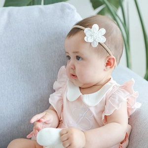 Close-up of baby girl wearing beige floral lace headband and pink cotton dress with embroidery