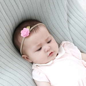 Detailed view of baby headband with pink felt flower and golden leaf on knit blanket
