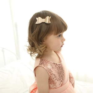 Detailed view of golden lychee texture bow hair clip worn by a young girl on a white backdrop