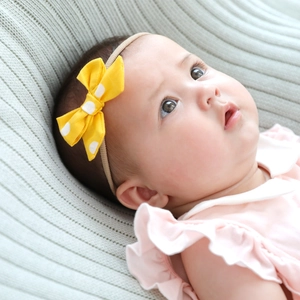 Close-up of yellow polka dot bow headband on baby with soft nylon elastic band detail