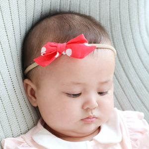 Detail of baby headband featuring a red polka dot bow on a soft elastic skin-tone strap