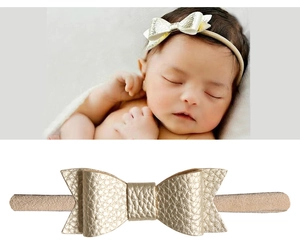 Détail d'un bandeau bébé avec un nœud en similicuir doré sur une sangle en nylon doux