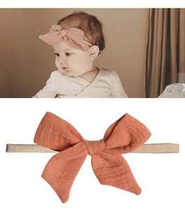 Detail of baby headband with large clay pink cotton bow and soft elastic strap on a white background