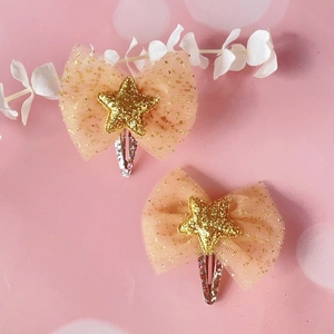 Macro shot of two light orange mesh bow hair clips with sparkling gold stars and silver metal BB clips