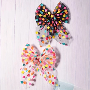 Detail of colorful polka dot mesh bow hair clips with long ribbons on white wood