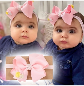 Détail d'un bandeau bébé à nœud rose avec perles blanches et accents floraux