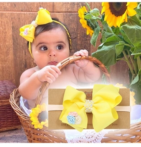 Détail d'un bandeau bébé à nœud jaune avec perles, strass et petites fleurs en tissu