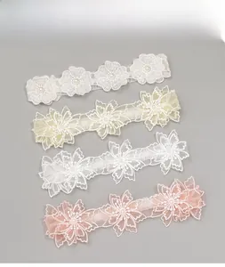 Détail de bandeaux en dentelle pour bébé avec trois fleurs brodées et perles en divers tons