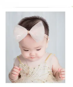 Détail d'un bébé portant un bandeau rose avec grand nœud en tulle et paillettes dorées