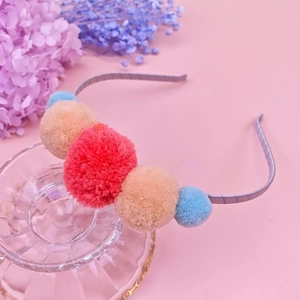 Dettaglio di un cerchietto argento con pompon di peluche colorati su sfondo rosa