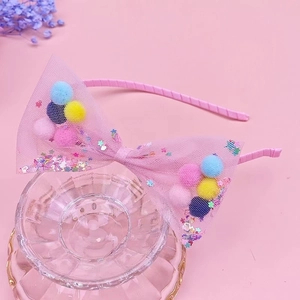 Dettaglio di cerchietto rosa con fiocco in rete, pompon colorati e paillettes su base vetro