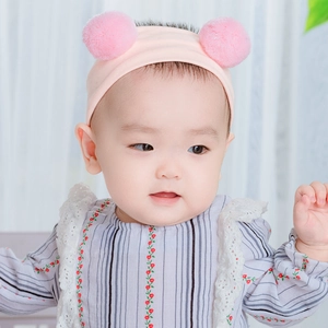 Rosa Baby-Strickstirnband mit weichen Bommeln, getragen von einem Baby im Hellen