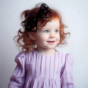 Detail of large black mesh hair bow with orange and purple stars on a young girl