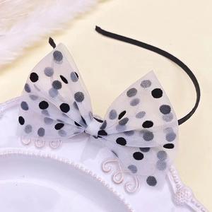 Close-up of elegant black polka dot mesh bow headband resting on white ceramic plate