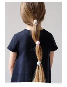 Detail view of pink pom pom hair tie with sequins on child's hairstyle for sweet look