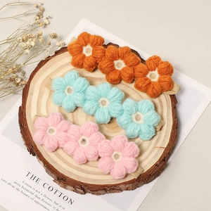 Detalle de tres pinzas de flores tejidas a mano en naranja, azul y rosa sobre madera