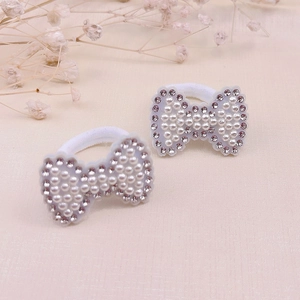Détail de chouchous en forme de nœud avec perles blanches et strass sur élastiques blancs