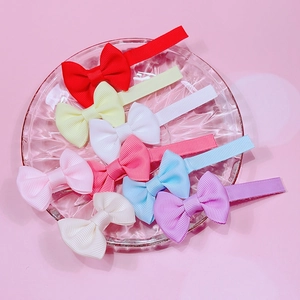 Gros plan de huit barrettes à nœuds colorés dans un plateau en verre sur fond rose