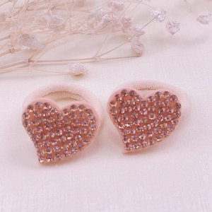 Detail of two heart-shaped elastic hair ties with sparkling pink rhinestones on fabric base