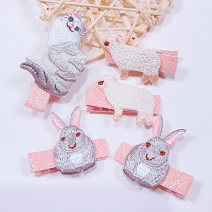 Detail of embroidered animal hair clips with cat, sheep, and rabbit motifs on pink glitter base