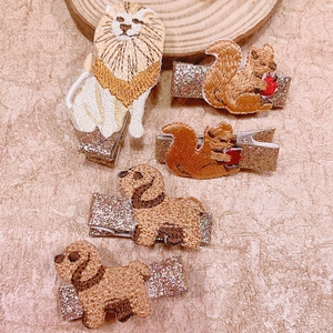 Close-up of embroidered animal hair clips with lion and squirrel motifs and glitter finish