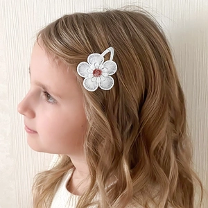 Dettaglio di un fermaglio per capelli a margherita in pizzo bianco ricamato su bimba