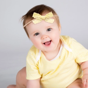 Close-up of baby girl wearing a bright yellow lace bow headband with elastic nylon band