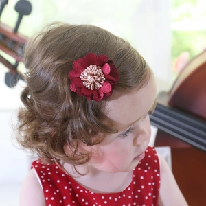 Gros plan d'une pince à cheveux fleur rouge pailletée portée par un enfant sur fond élégant
