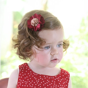 Détail d'une pince à cheveux fleur en tissu rouge faite main sur cheveux bouclés