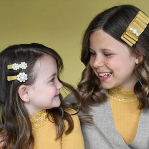 Detail of girls' yellow ribbon hair clips with white pearls worn by children in lifestyle setting
