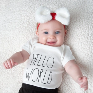 Detail shot of baby outfit set including white bodysuit with Hello World print and red bow