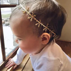 Detail of infant wearing a gold snowflake elastic headband near a wooden window