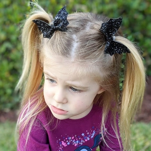 Toddler wearing sparkling black sequin bat wing hair clips for Halloween festivities
