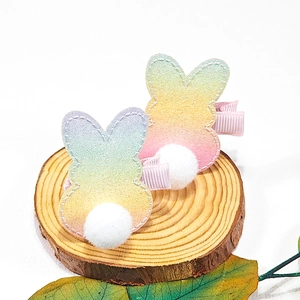 Makro-Detail von Regenbogen-Glitzer-Hasen-Haarspangen mit weißem Pompon und rosa Band