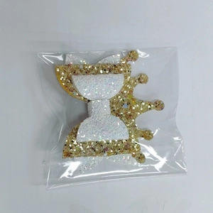 Detail of a sparkling gold glitter crown bow hair clip packaged in a clear OPP bag