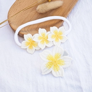 Detail of white crochet flower baby headband and matching hair clip set on a wooden tray