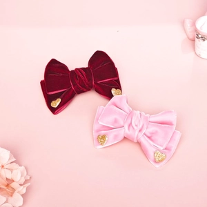 Detalle de lazos de terciopelo rojo y rosa con lentejuelas de corazón doradas sobre rosa